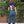 Person wearing a black tshirt with white text and blue jeans standing on a wooden deck with trees in the background.