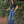 Person standing on a wooden deck wearing a black tshirt and blue jeans with trees in the background