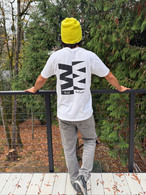 Person wearing a white sweatshirt with black text and a yellow beanie, standing on a wooden platform with trees in the background.